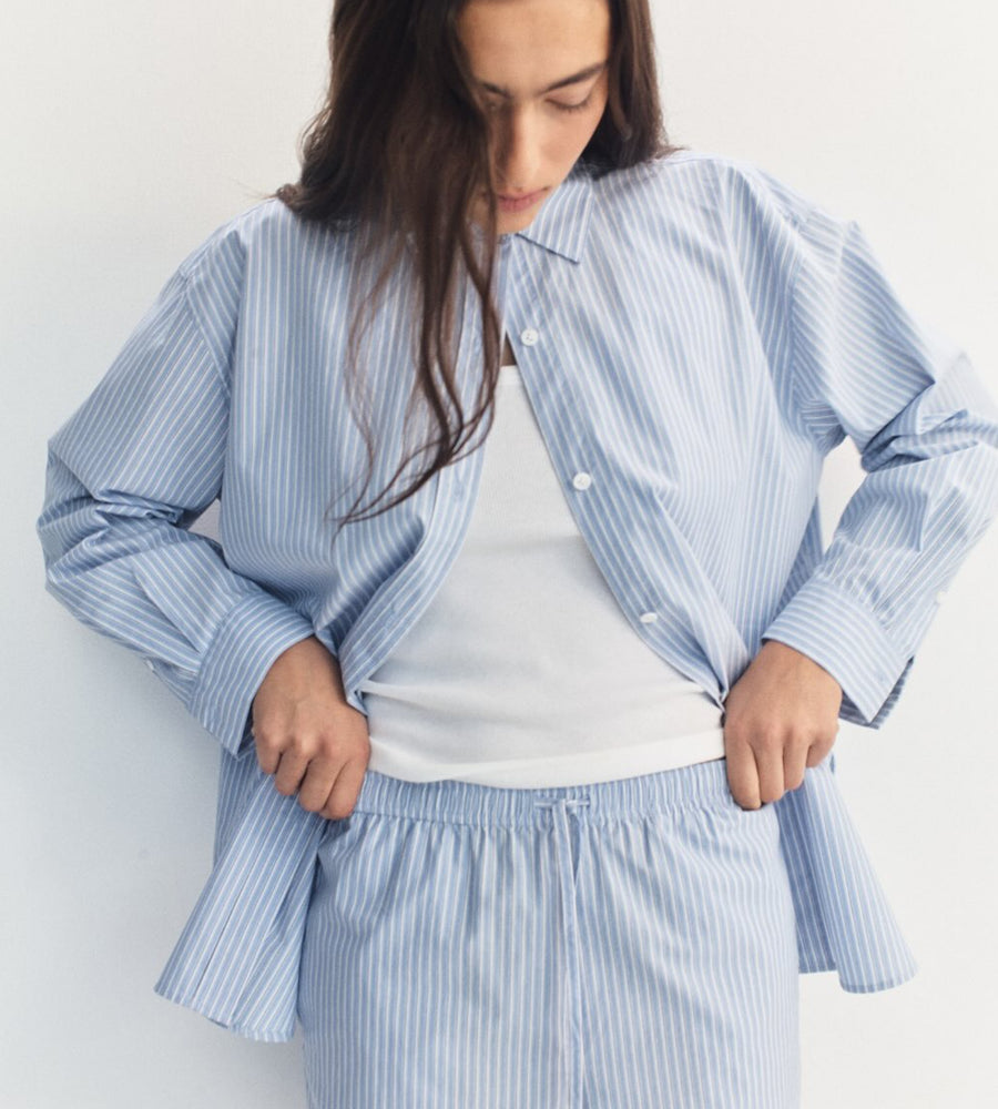 Woman wearing a blue striped pajama set against a white background