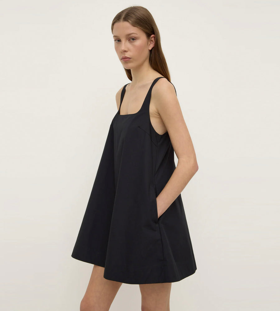 Woman wearing a black sleeveless dress against a plain background