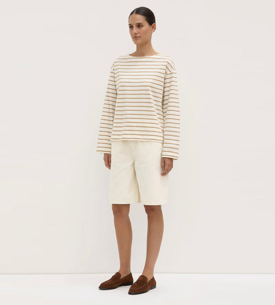 Person wearing a striped sweater and white pants on a plain background