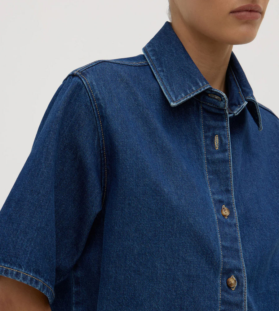 Close-up of a person wearing a blue denim shirt on a plain background