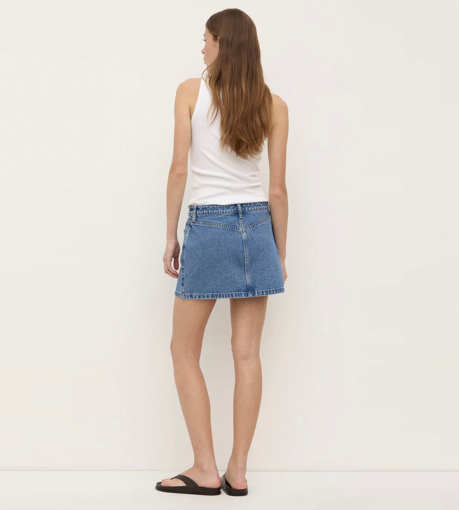 Woman wearing a white tank top and blue denim skirt on a white background