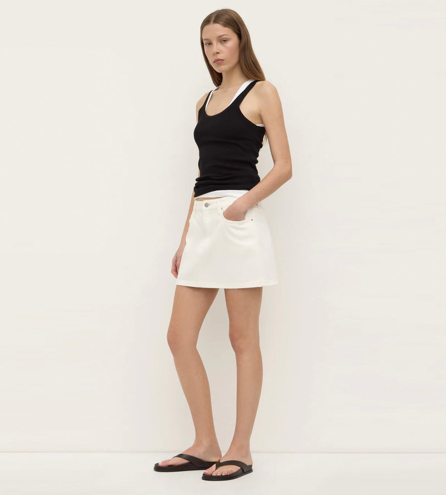 Woman wearing a black tank top and white shorts against a plain background