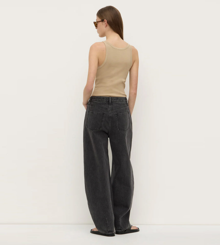 Person wearing a beige tank top and black jeans against a white background