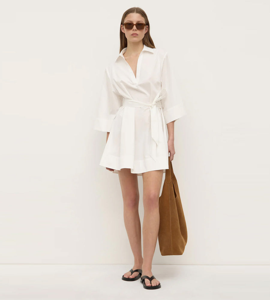 Woman wearing a white dress holding a brown bag against a white background