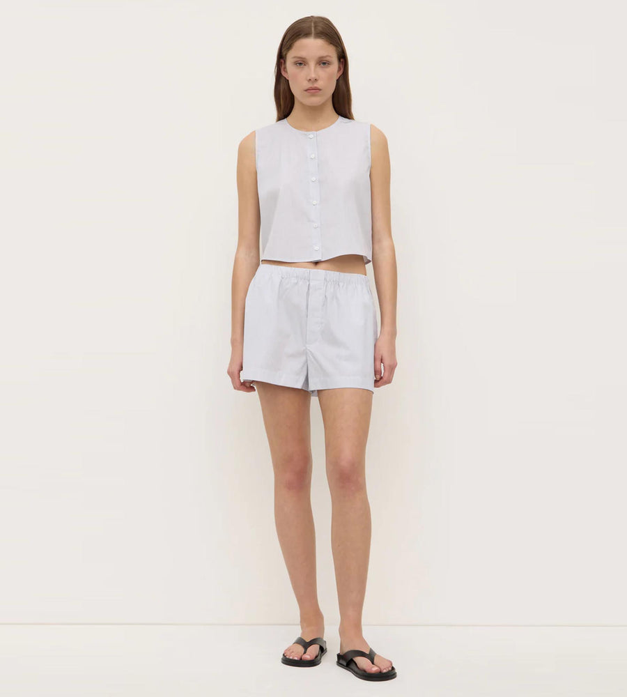 Woman wearing a sleeveless white top and shorts on a plain background