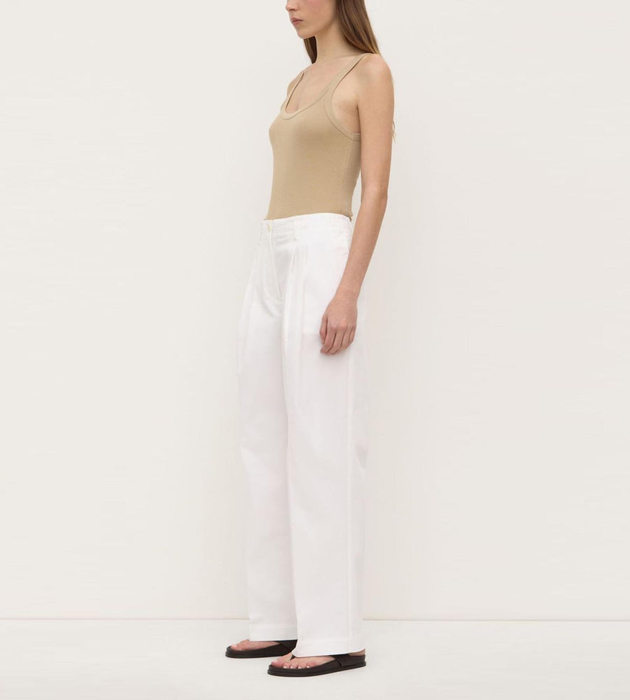 Woman wearing a beige top and white pants on a plain background