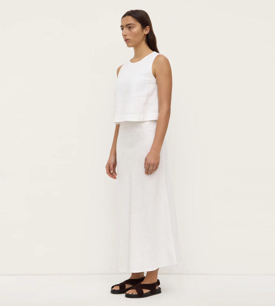 Woman wearing a white sleeveless top and wide-leg pants on a plain background