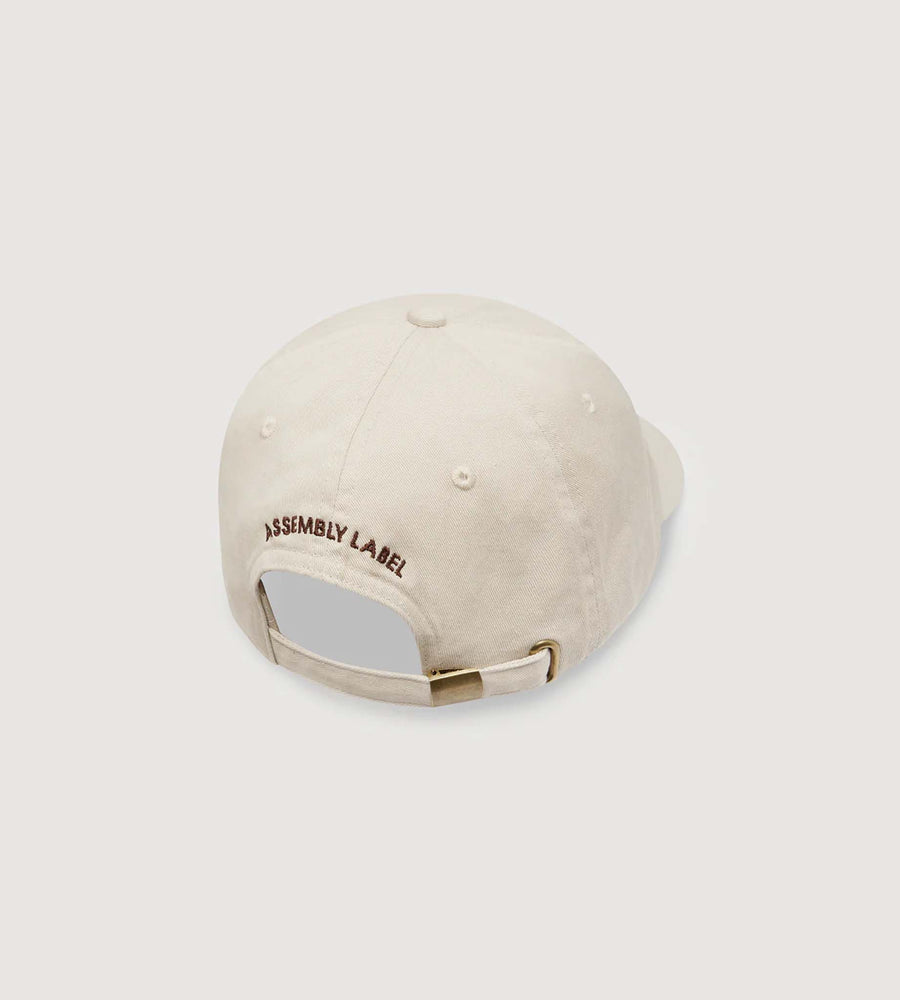 Beige cap with 'Assembly Label' logo on a light gray background