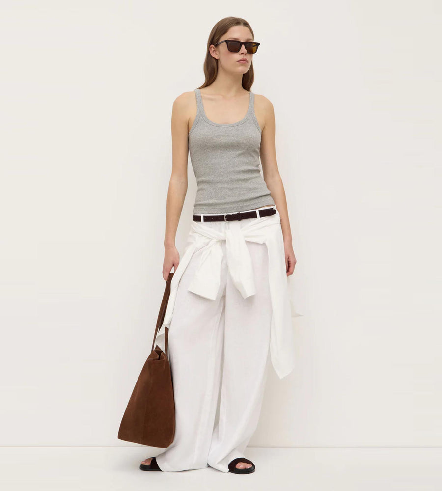 Woman wearing a gray tank top and white pants with a brown bag on a white background