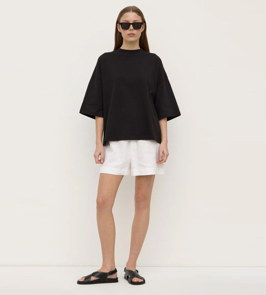 Person wearing a black oversized top and white shorts on a plain background