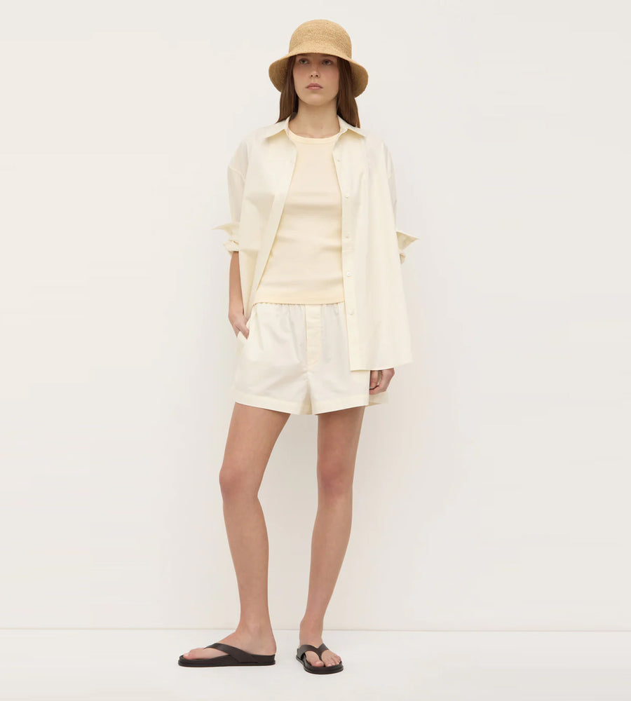 Person wearing a light-colored outfit with a hat on a white background