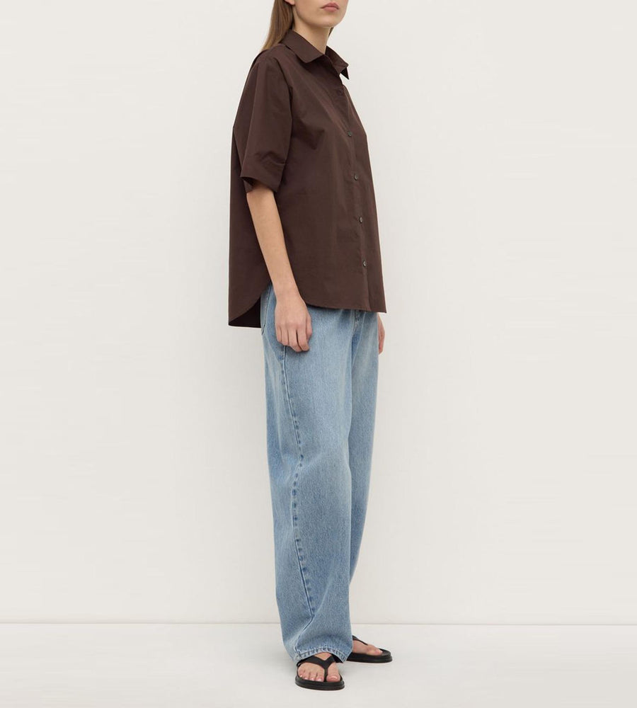 Person wearing a brown shirt and blue jeans against a white background