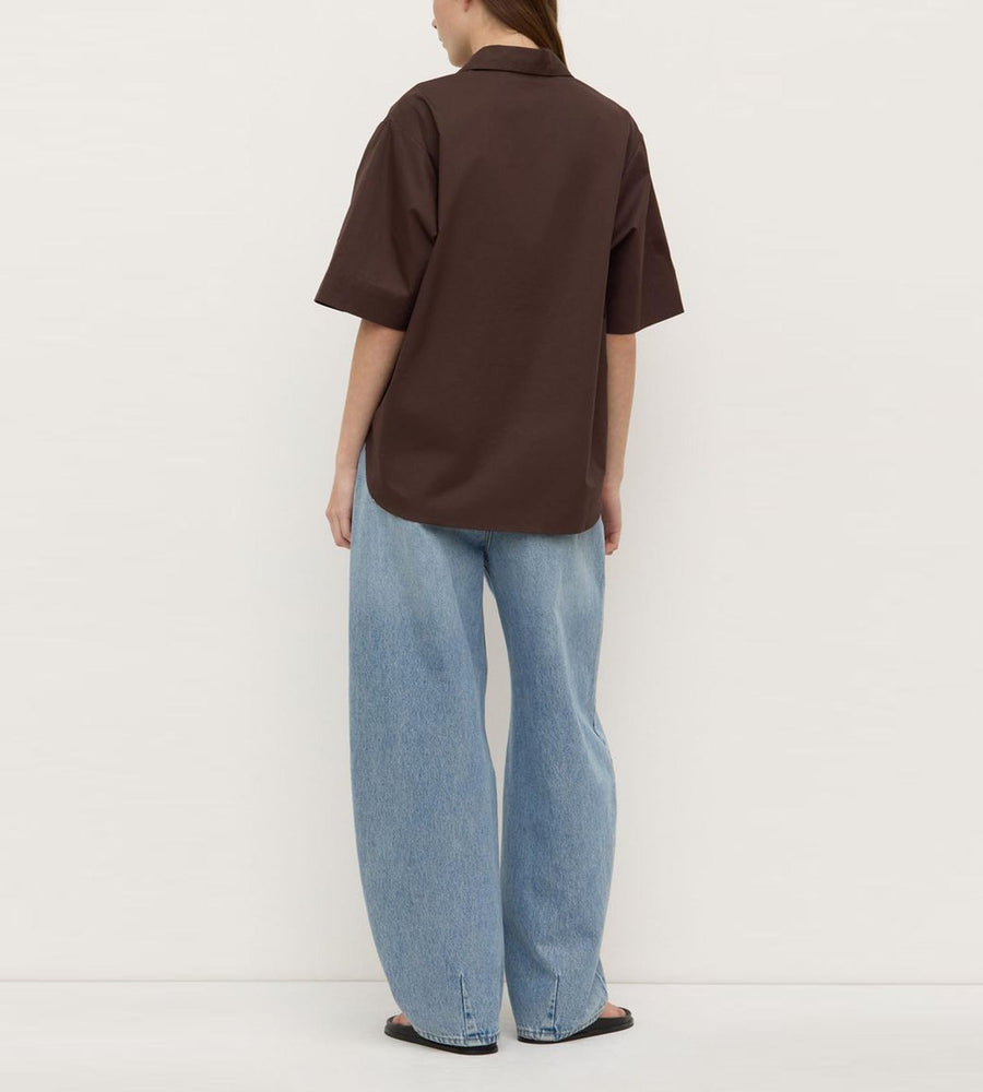 Person wearing a brown shirt and blue jeans against a white background