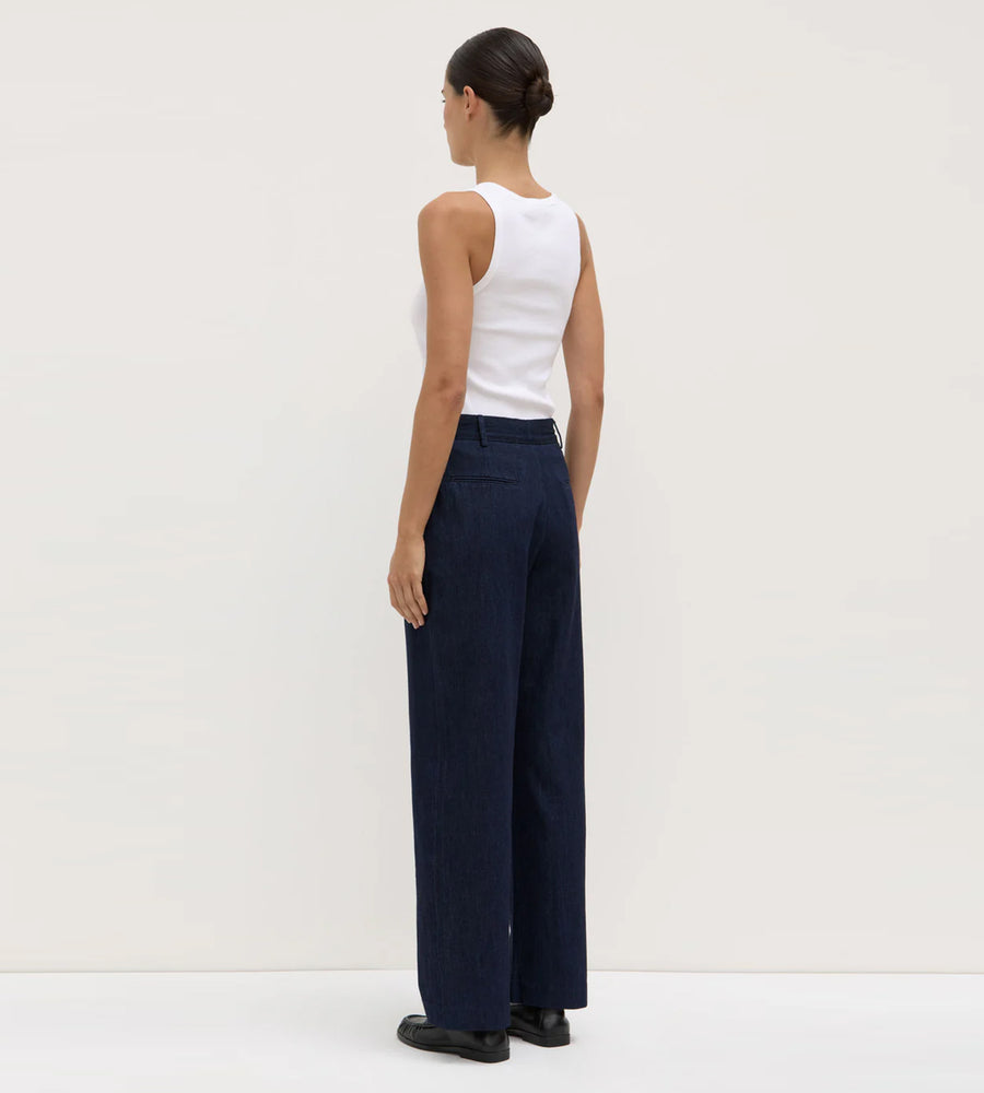 Woman wearing navy wide-leg pants and a white top on a plain background