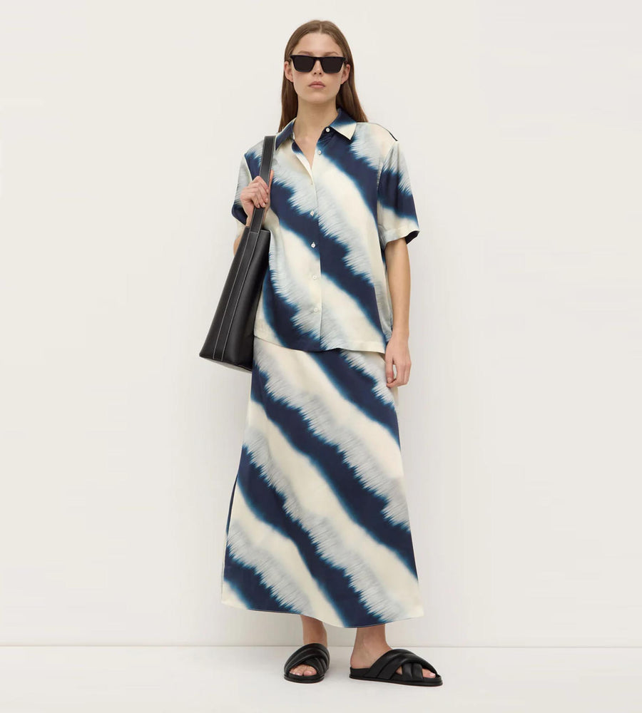 Person wearing a blue and white tie-dye outfit with sunglasses and a black bag on a white background