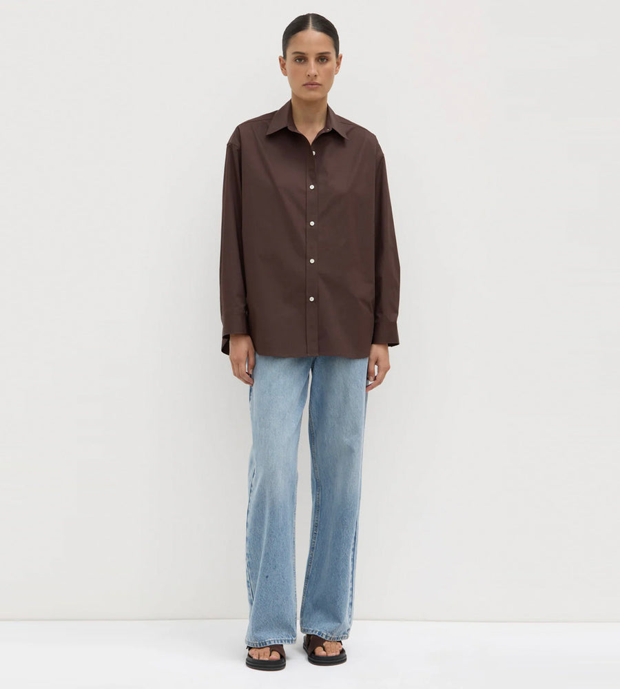 Person wearing a brown shirt and light blue jeans on a white background