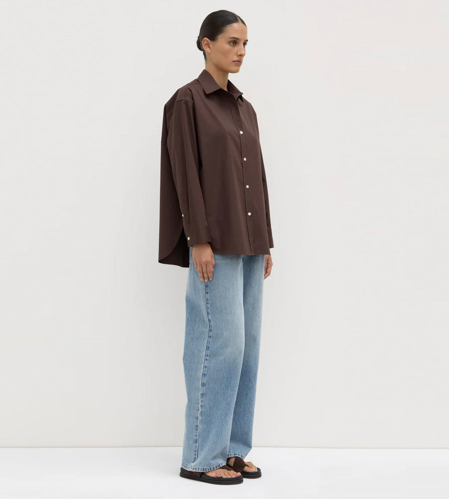 Person wearing a brown shirt and blue jeans against a white background