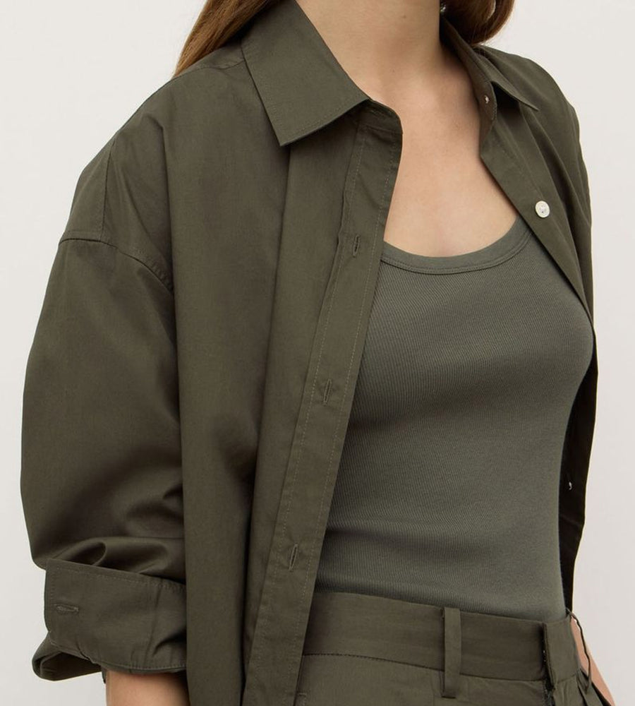 Person wearing an olive green jacket over a matching top on a plain background