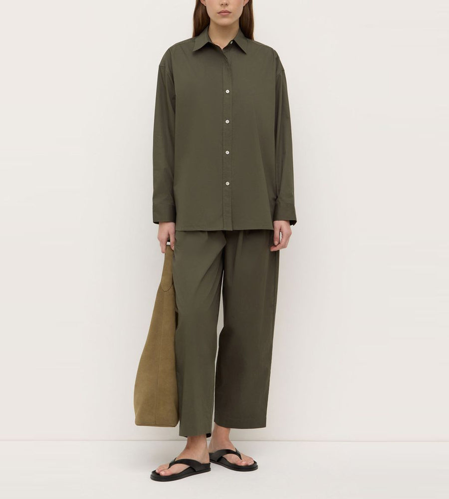 Person wearing an olive green outfit with a shirt and wide-leg pants against a white background