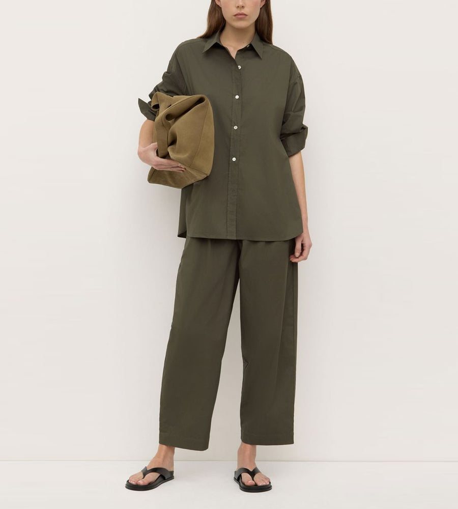 Person wearing an olive green outfit holding a matching jacket against a white background