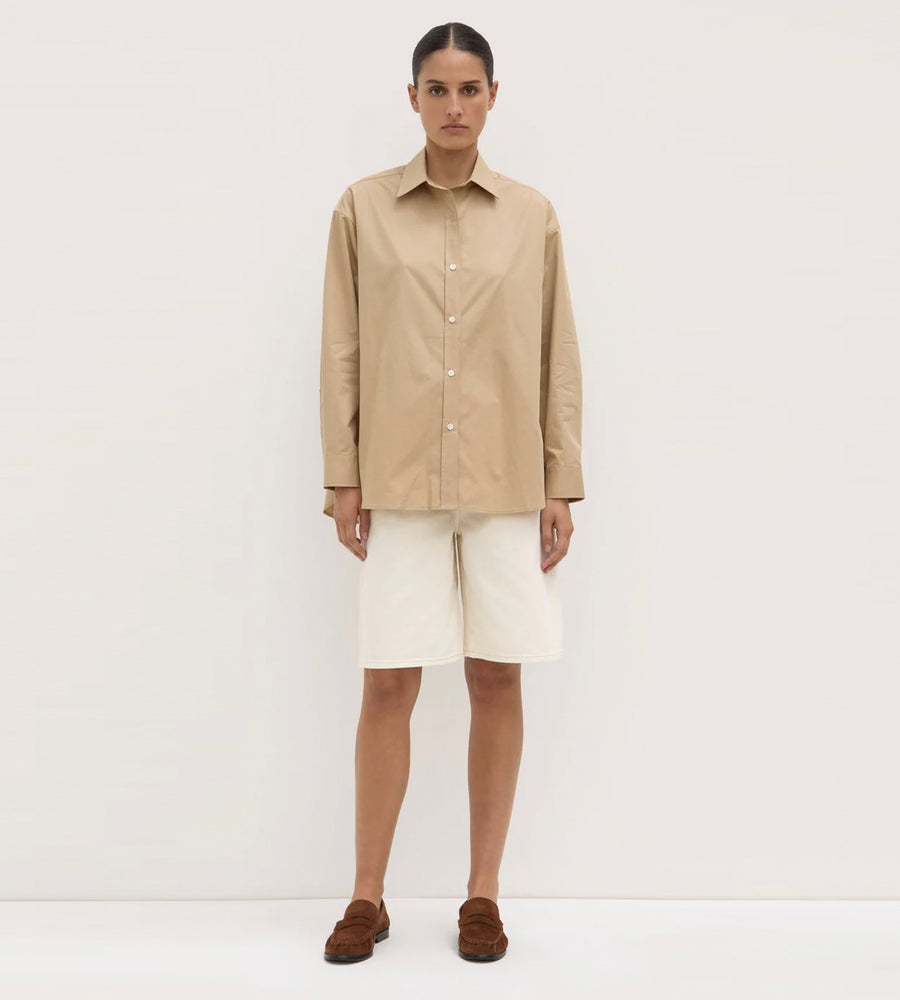Person wearing a beige shirt and white pants on a plain background