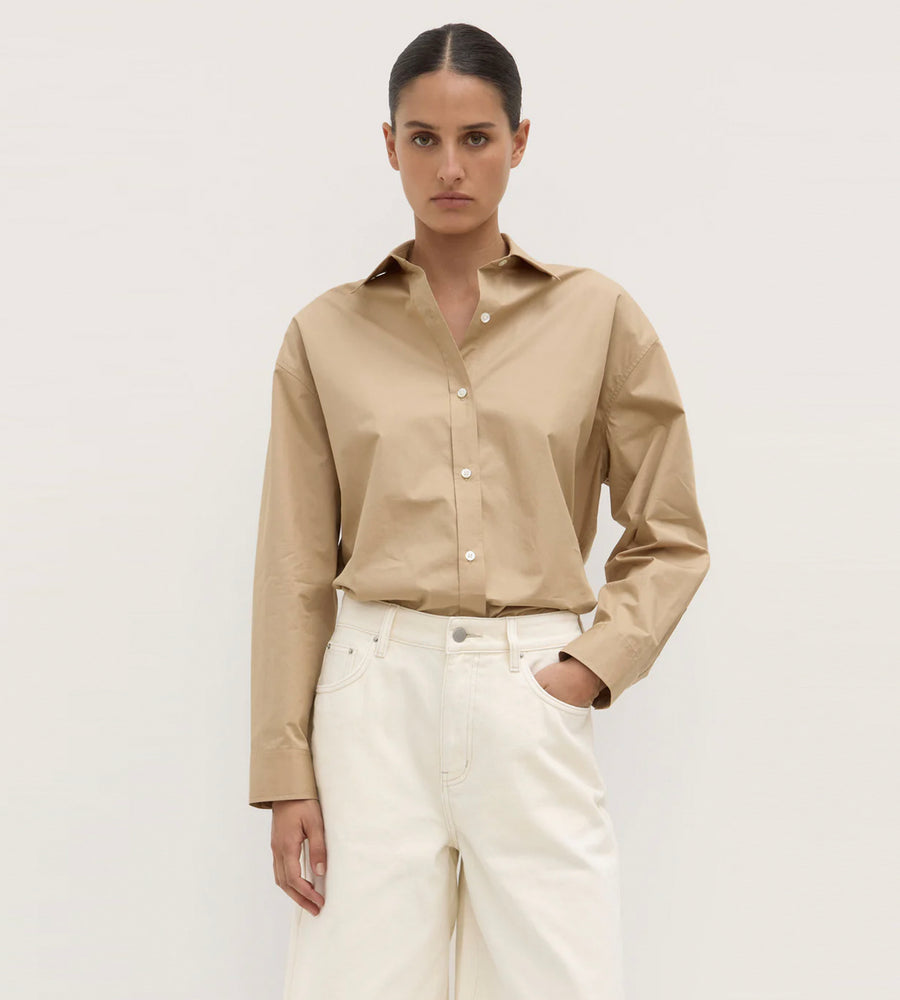 Woman wearing a beige shirt and white pants against a plain background