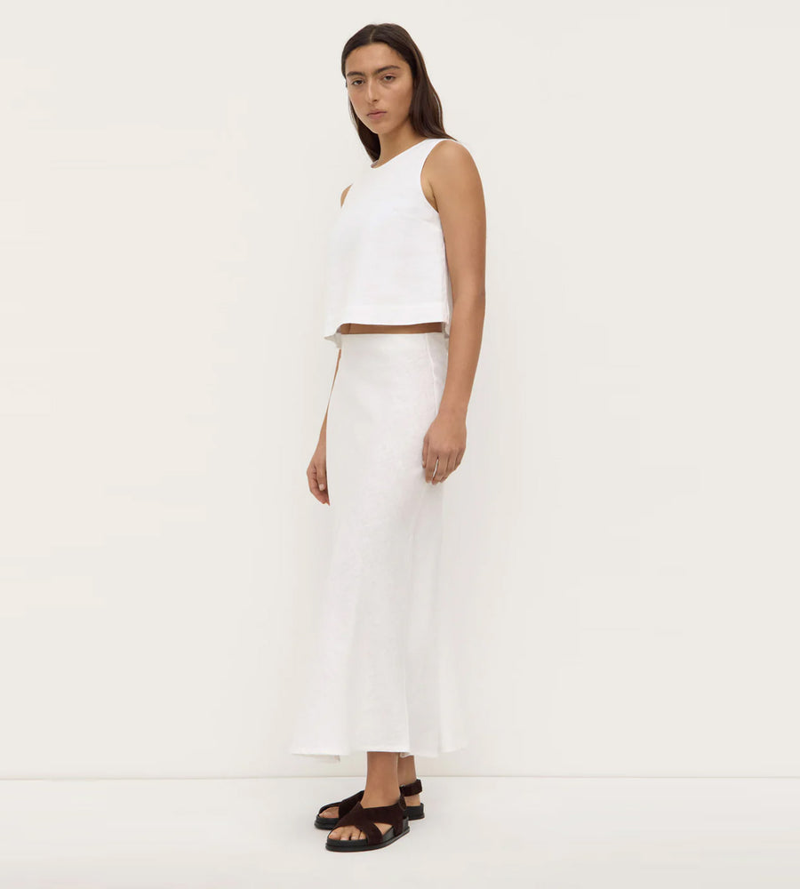 Woman wearing a white sleeveless top and white pants on a plain background
