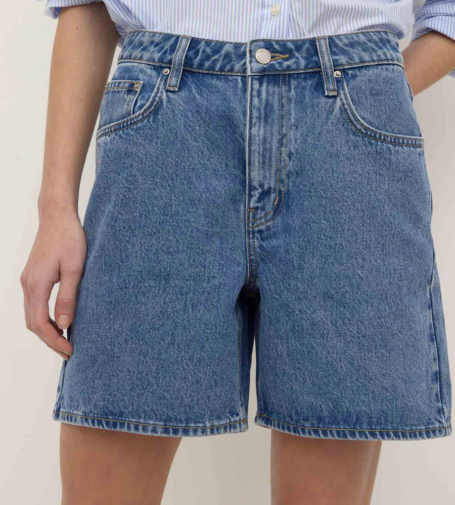 Blue denim shorts worn by a person on a plain background