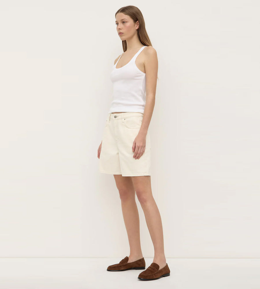 Woman wearing a white tank top and cream shorts on a plain background