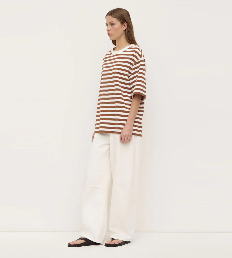 Woman wearing a striped shirt and white pants on a plain background
