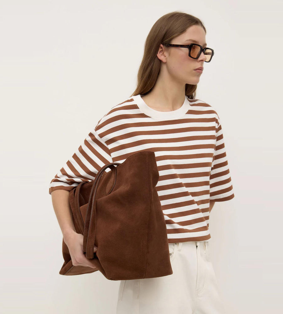 Woman wearing a brown and white striped shirt holding a brown bag against a plain background