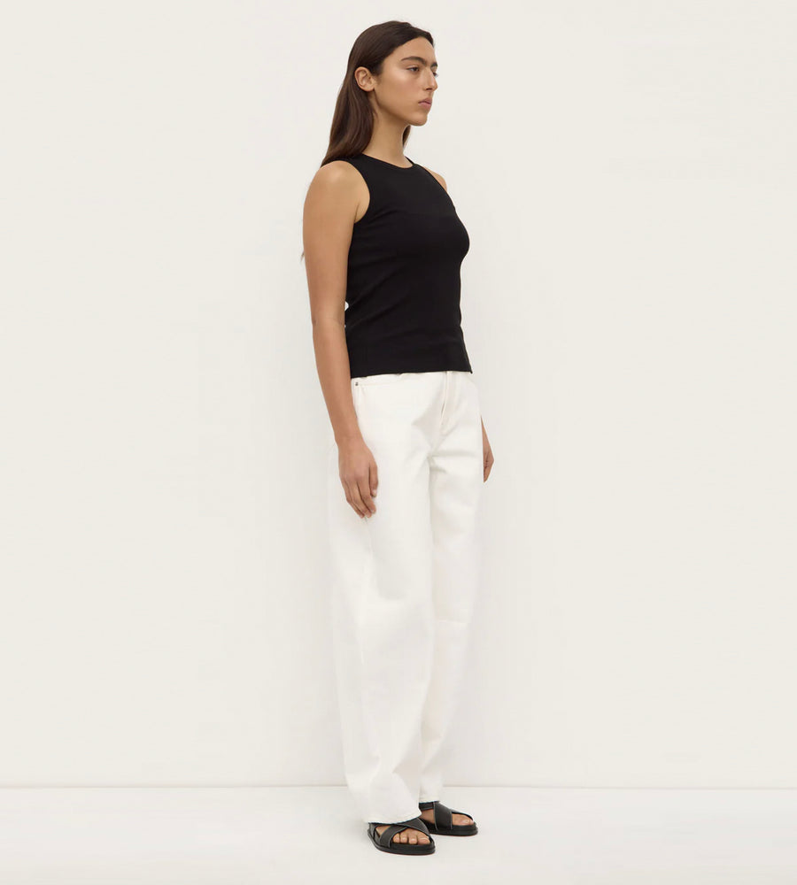 Woman wearing a black sleeveless top and white pants on a plain background