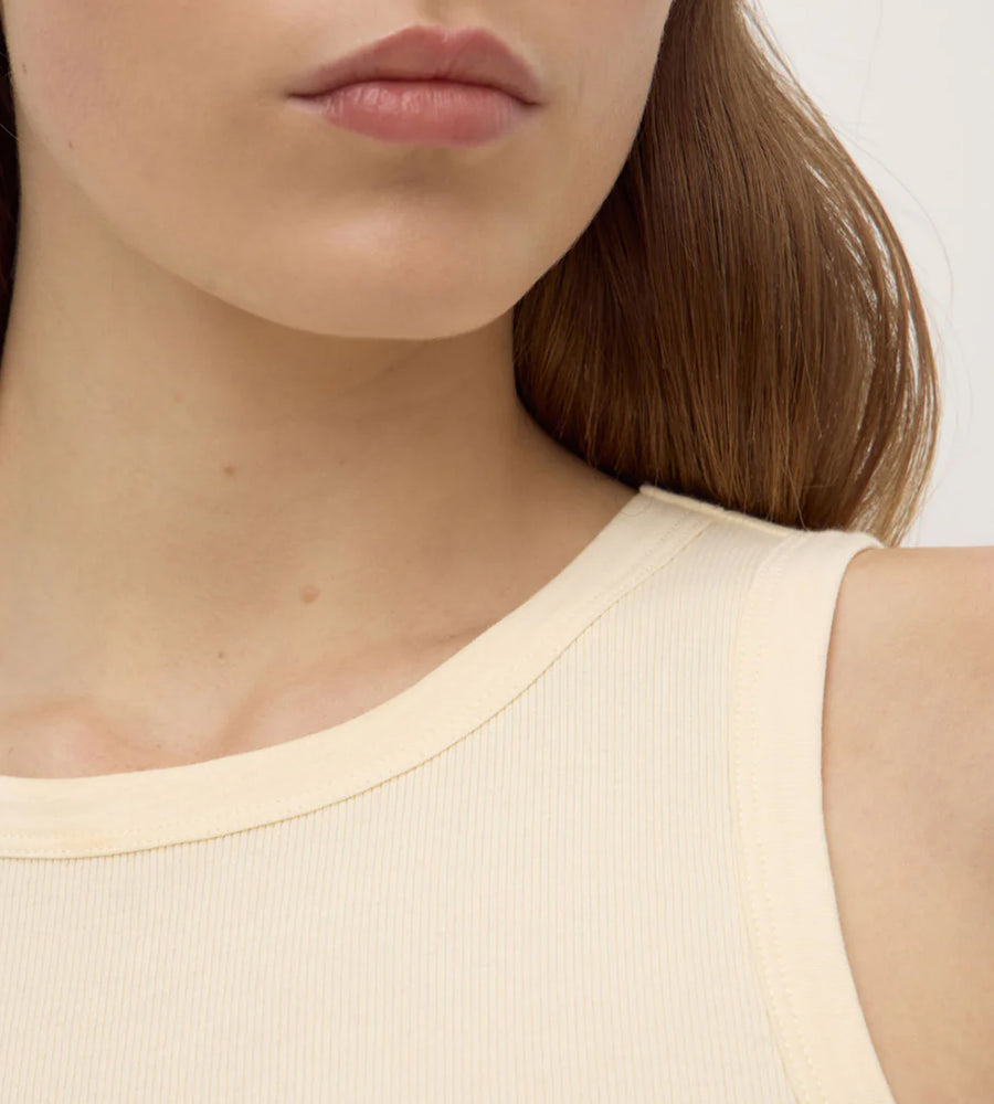 Close-up of a person wearing a beige sleeveless top with a plain background