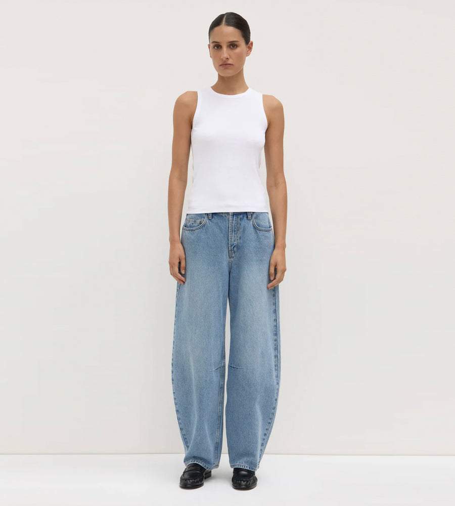 Person wearing a white sleeveless top and light blue jeans on a plain background