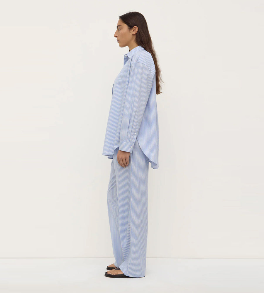 Woman wearing a light blue striped shirt and pants on a white background