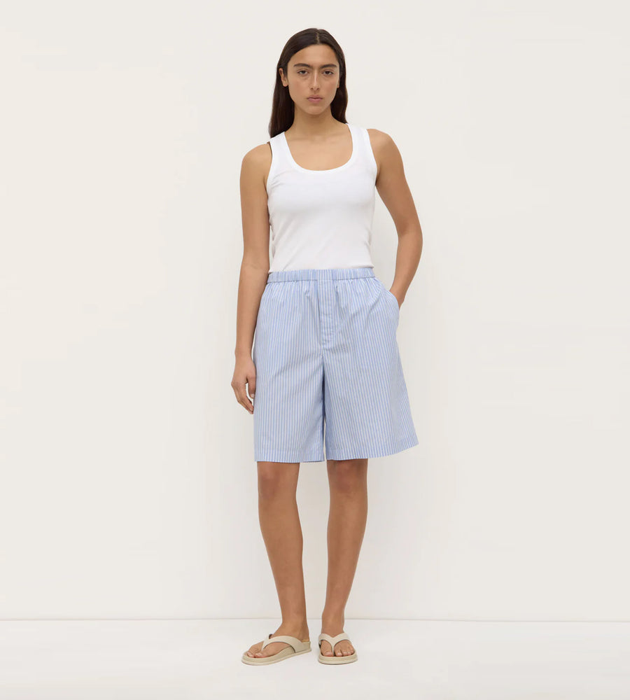 Woman wearing a white tank top and light blue checkered shorts on a white background
