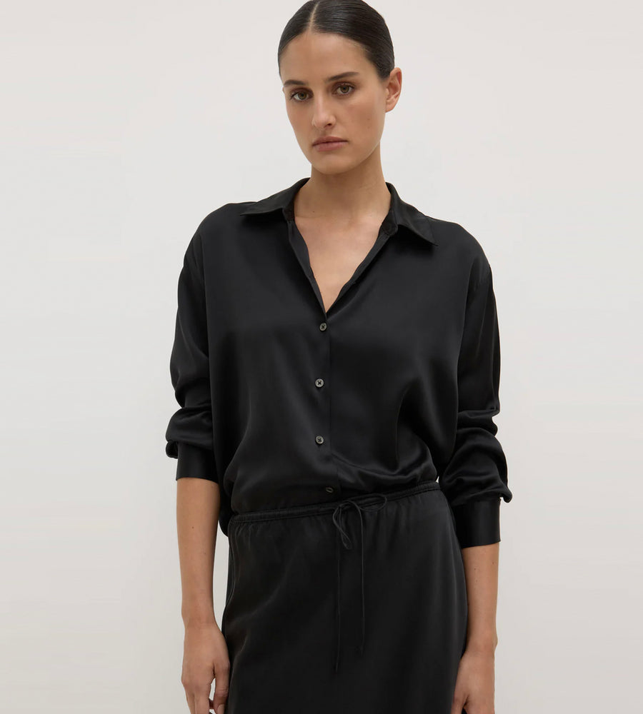 Woman wearing a black shirt and skirt set against a plain background