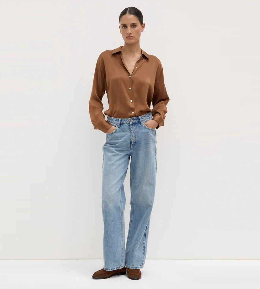 Person wearing a brown shirt and light blue jeans on a white background