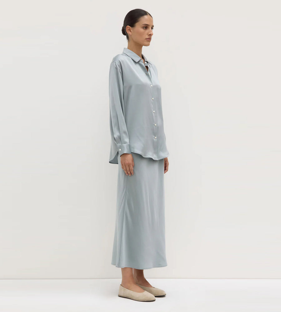 Woman wearing a light blue satin shirt and skirt set on a white background