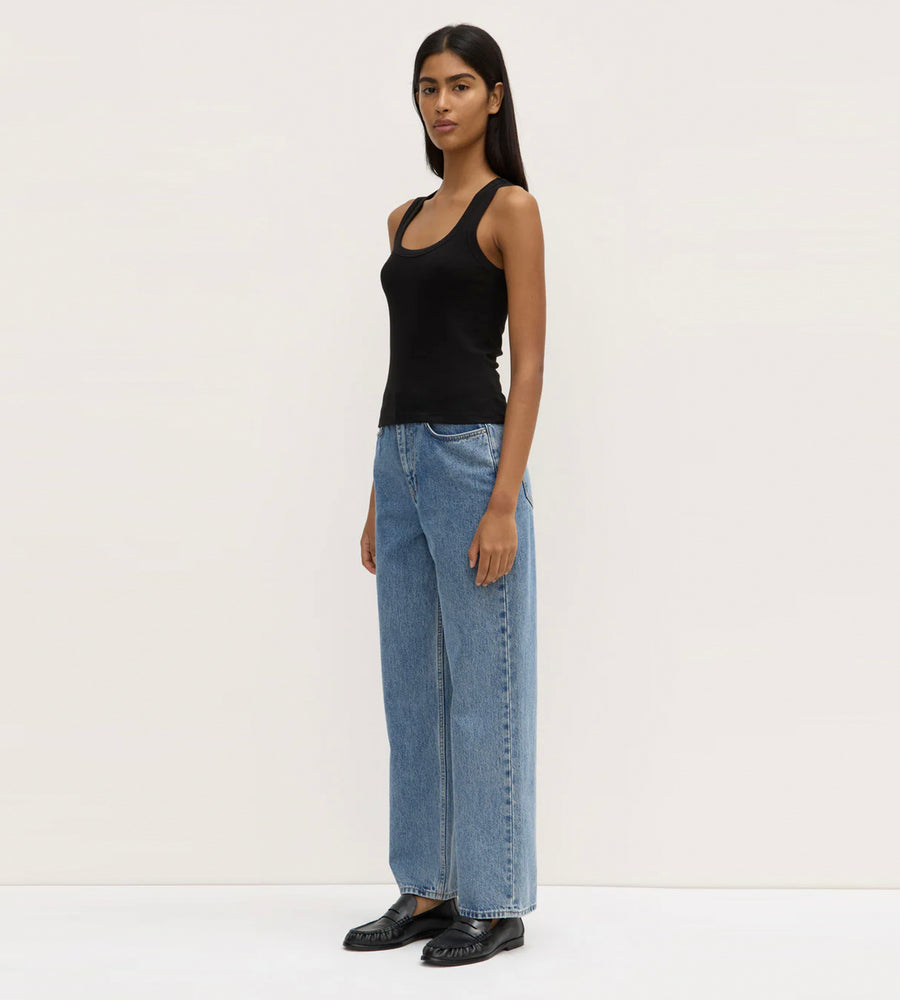 Woman wearing a black tank top and blue jeans on a white background