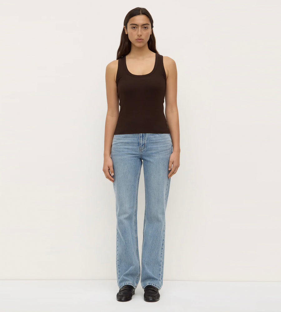 Person wearing a black tank top and light blue jeans on a white background