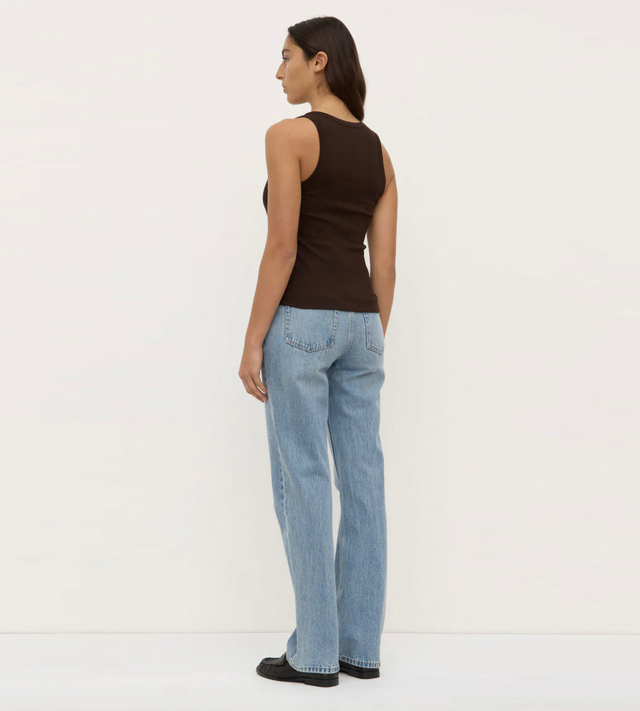Woman wearing a brown tank top and light blue jeans against a white background