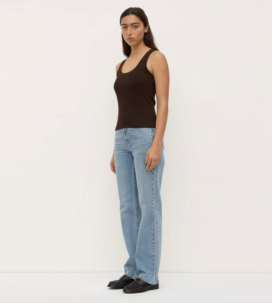 Person wearing a black tank top and light blue jeans on a white background