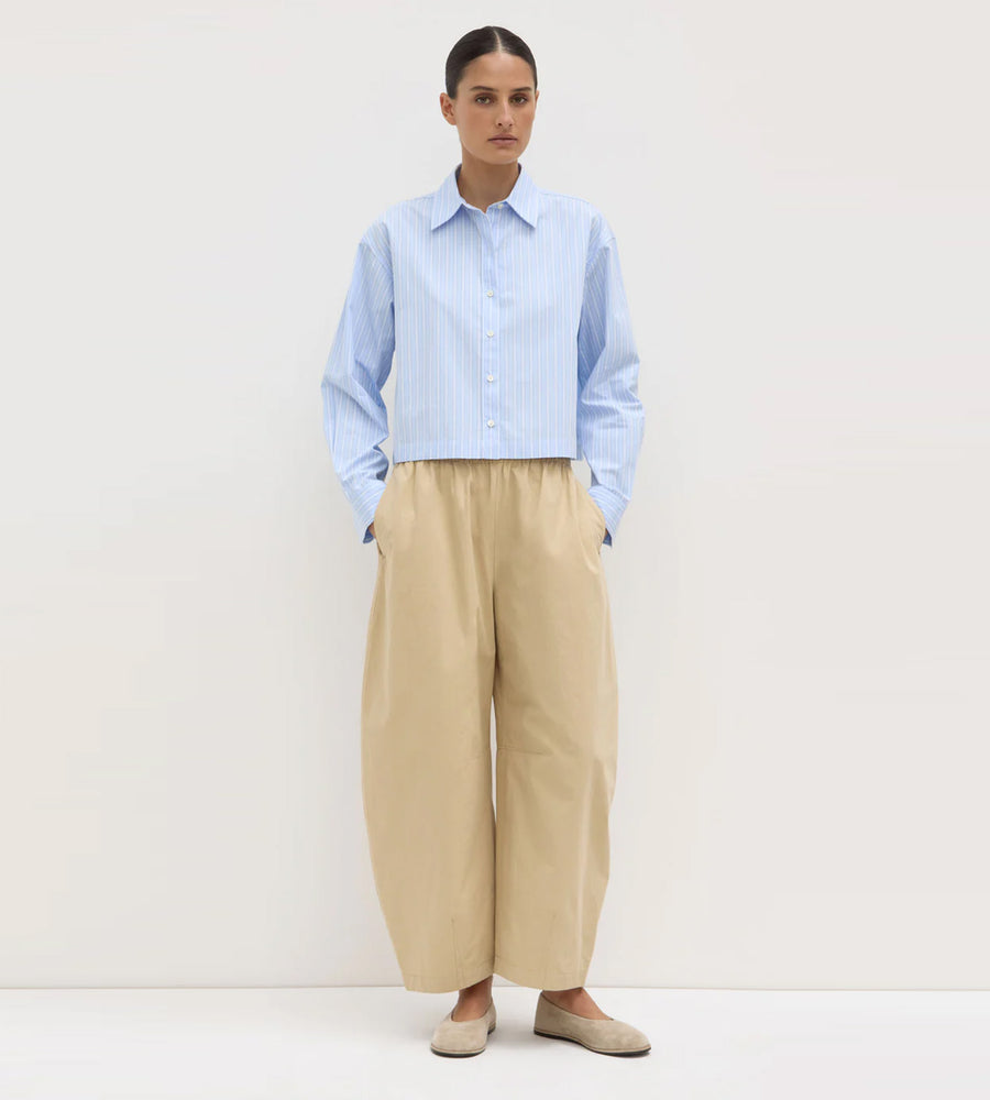 Person wearing a light blue checkered shirt and beige pants on a white background