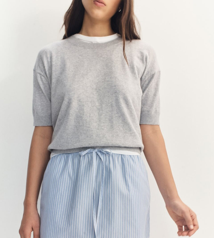 Person wearing a gray short-sleeve top and light blue striped pants on a white background