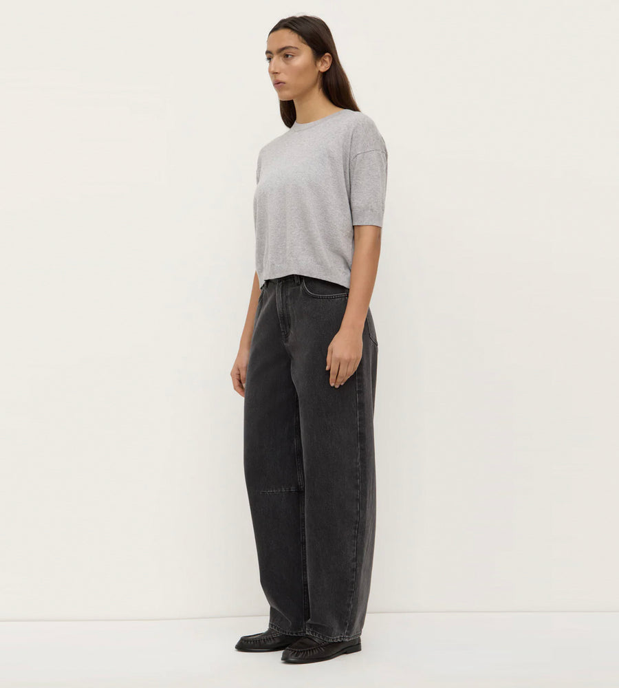 Woman wearing a gray top and black pants against a white background