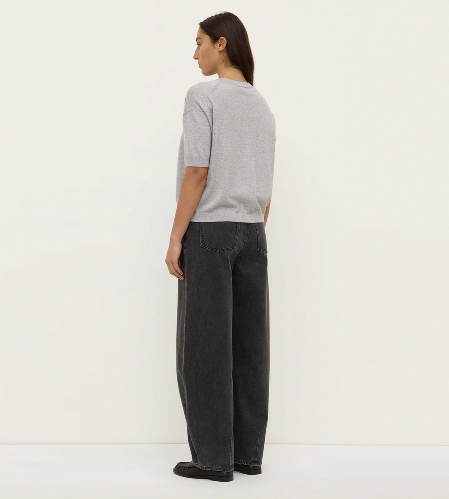 Person wearing a gray t-shirt and dark pants against a white background