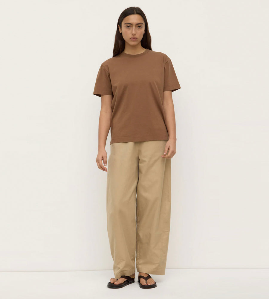 Person wearing a brown t-shirt and beige pants on a white background