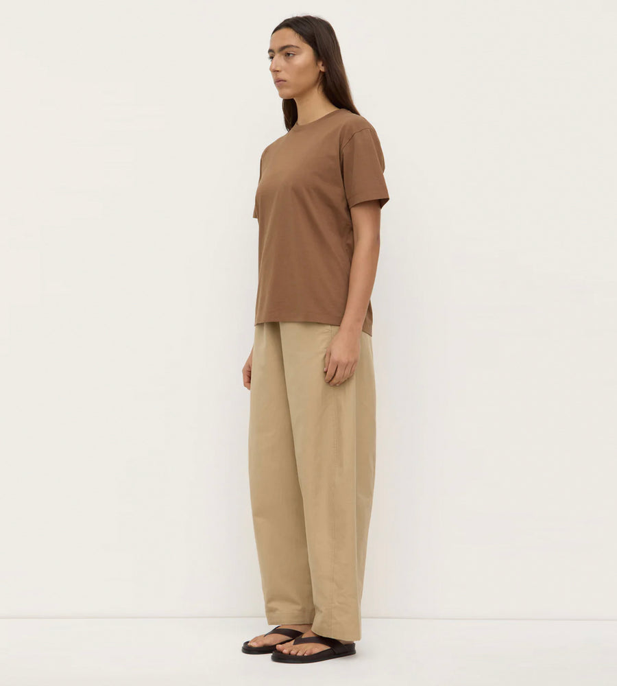 Woman wearing a brown t-shirt and beige pants against a white background