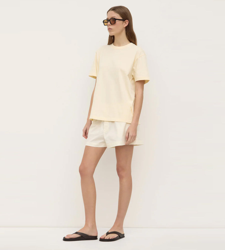 Person wearing a light yellow t-shirt and white shorts against a plain background
